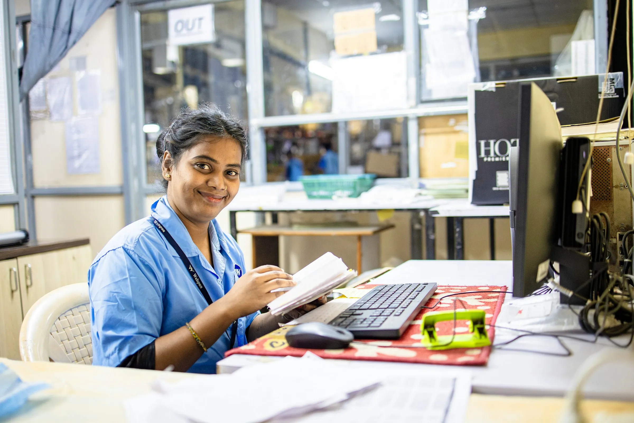 A woman at her office desk writing in a register beside her computer