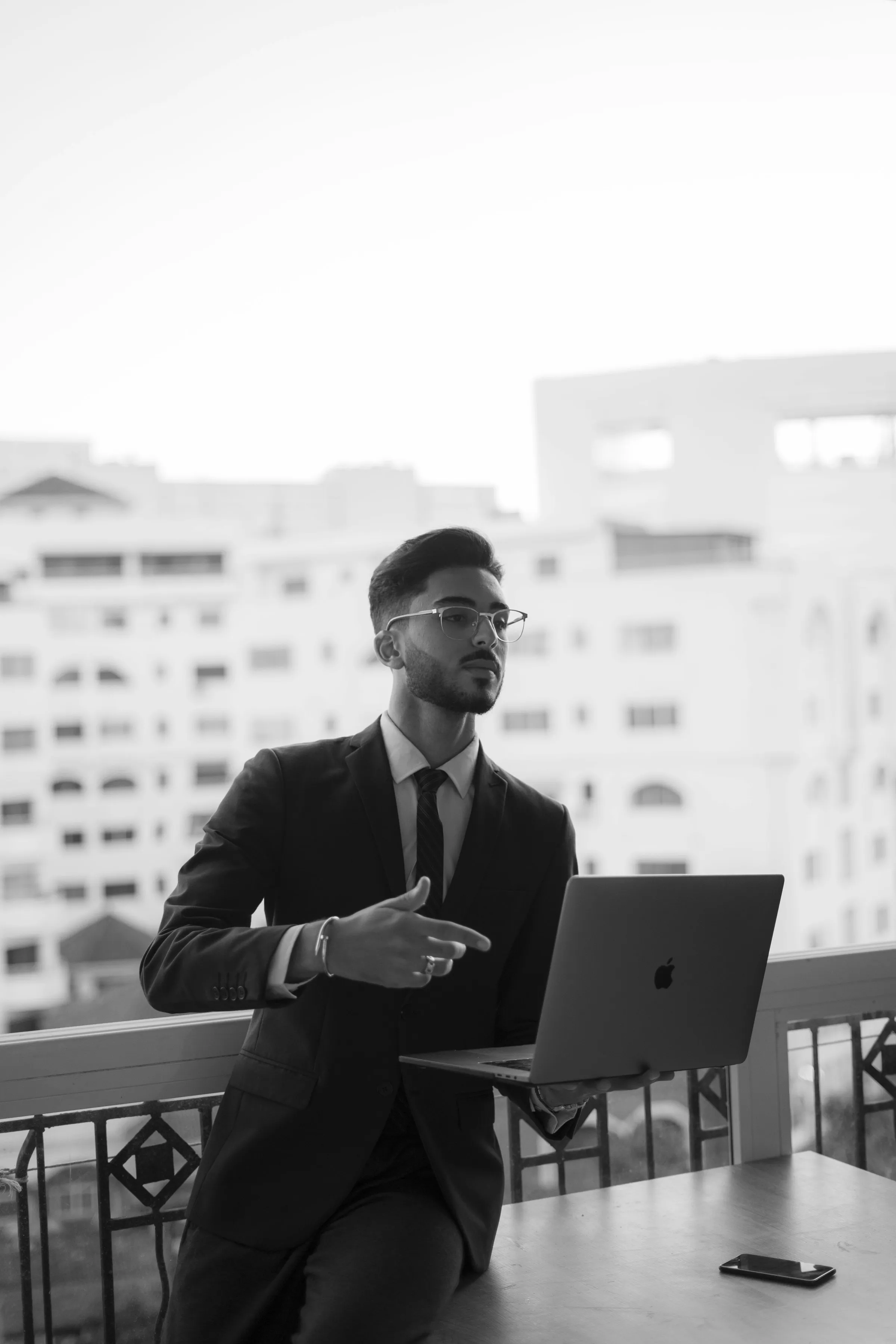 A man in a suit working at a laptop by a window, in black and white