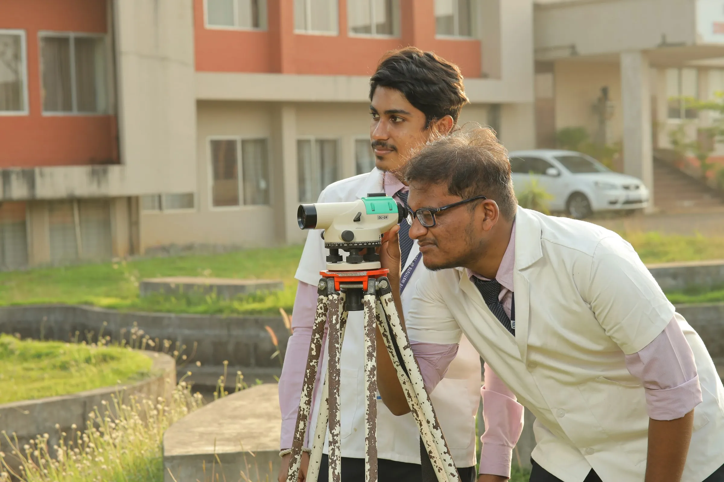 A site engineer taking a level reading with a surveying instrument while a colleague watches