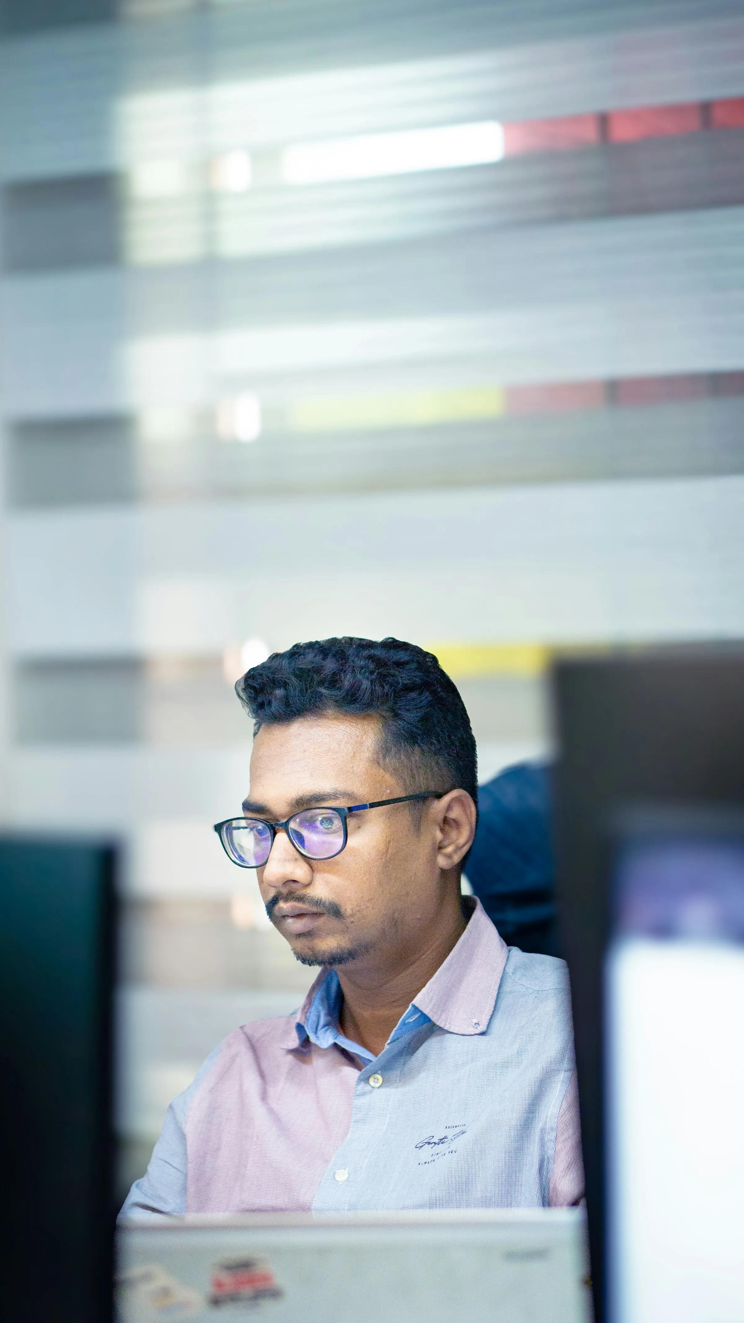 A man in glasses reading his screen closely at an office desk